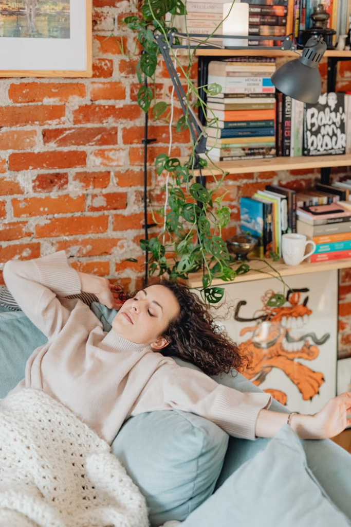 Caucasian woman relaxing with eyes closed on a comfortable sofa in a cozy room with bookshelves.