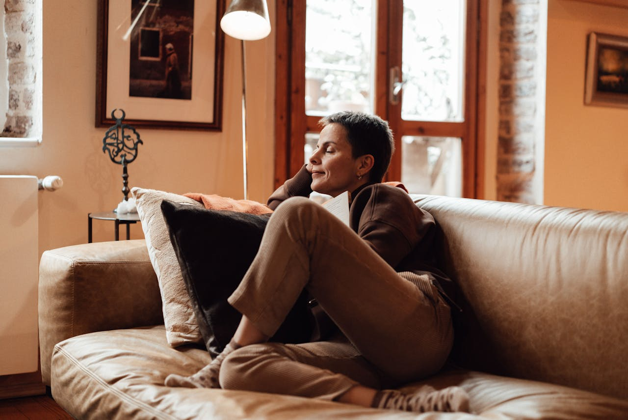 A woman relaxing on a leather couch in a cozy living room, reading peacefully.
