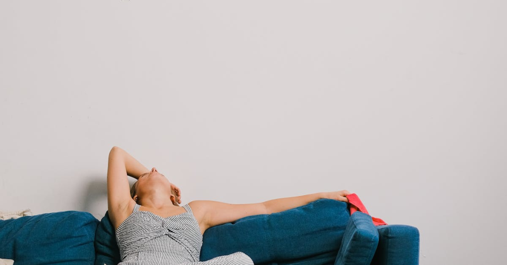 Unrecognizable exhausted woman with rag touching head while leaning back on couch after housework in living room